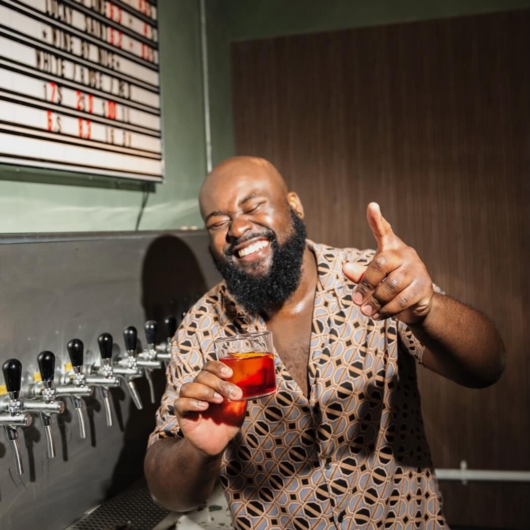 A staff member is grinning while holding a freshly prepared Negroni behind the bar at Trickle